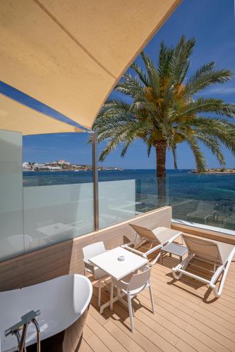 a deck with tables and chairs and a palm tree at Hotel Torre del Mar - Ibiza in Playa d'en Bossa