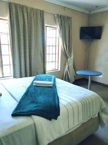 a bedroom with a large bed with a blue blanket on it at Kaste Guest House Edenvale in Edenvale