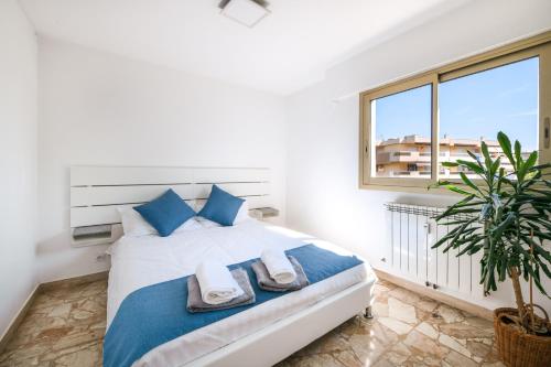 a bedroom with a bed with blue pillows and a window at Résidence méditerranée - Beachfront - Sun and Seaview - Pool - Private Parking in Cagnes-sur-Mer