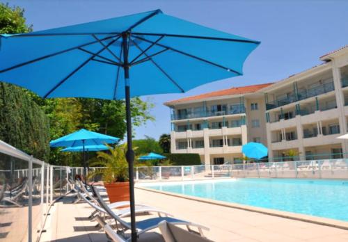 a pool with blue umbrellas and chairs next to a hotel at Situation idéale Piscine Parking Wifi Gare Plage Golf in Ciboure