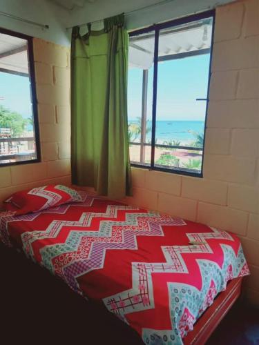 a bed in a room with two windows and a bedspread at La palmera zorritos in Tumbes
