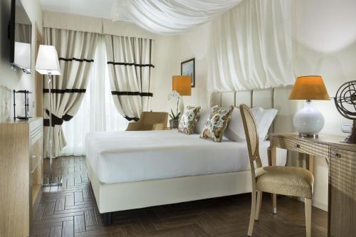 Erbavoglio Hotel في ريميني: غرفة نوم بسرير ابيض ومكتب وكرسي