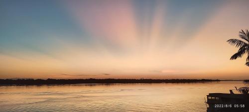 a sunset over a body of water with a palm tree at EL DORADO POUSADA in Barcelos