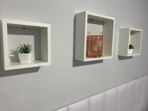 two white shelves on a wall with plants in them at Confortável Apartamento em Bagé in Bagé