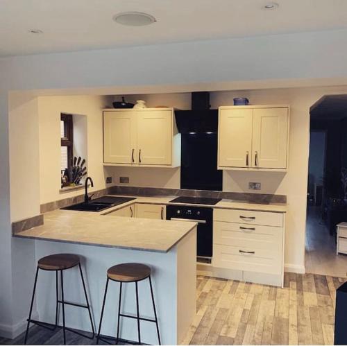 a kitchen with white cabinets and two bar stools at 3 bedroom home in Nottage, Porthcawl in Nottage