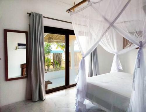 a bedroom with a white canopy bed and a window at Casa do Índico in Praia do Tofo