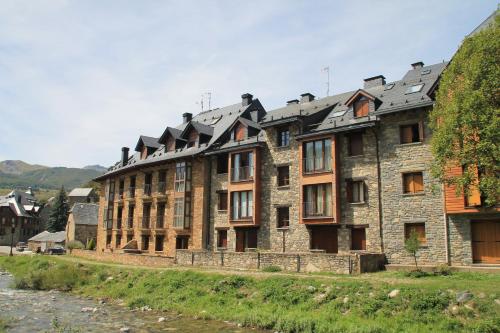 un gran edificio de piedra con muchas ventanas junto a un río en Sallent de Gállego - Formigal - Pirineos Sur, en Sallent de Gállego