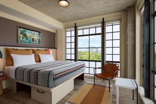 a bedroom with a bed and a chair and windows at Moxy Charleston Downtown in Charleston