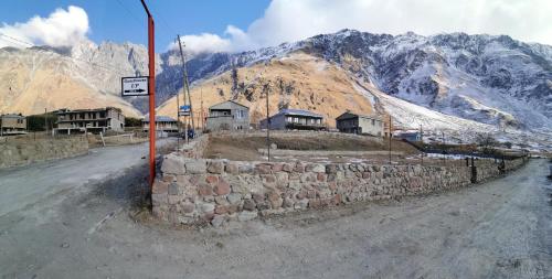 a stone wall next to a road with mountains at UP Holiday Home in Stepantsminda