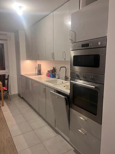 une cuisine avec des appareils en acier inoxydable et des armoires blanches dans l'établissement Chambre individuelle dans un appartement à 37 de champs élysées, à Sartrouville