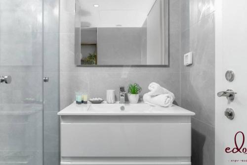 La salle de bains blanche est pourvue d'un lavabo et d'une douche. dans l'établissement דירה יוקרתית 100 מטר מהים - By Edom, à Eilat
