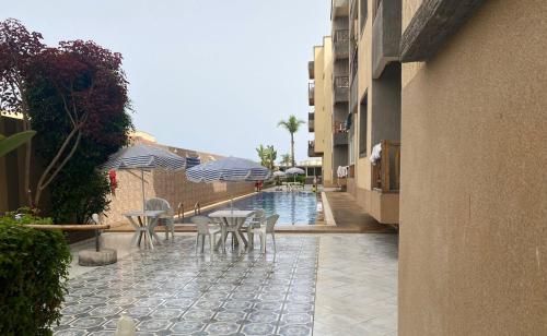 eine Terrasse mit Tischen und Sonnenschirmen neben einem Pool in der Unterkunft Eden Appartement avec Piscine Et Salle de Sport in El Jadida