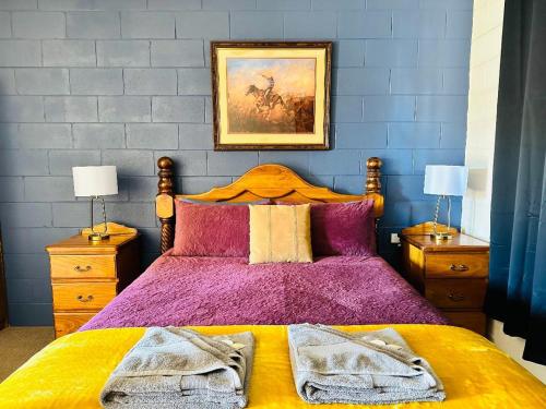 ein Schlafzimmer mit einem Bett mit violetter Bettwäsche und einem Gemälde an der Wand in der Unterkunft Flinders Ranges Motel - The Mill in Quorn