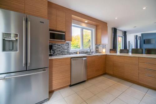 a kitchen with wooden cabinets and a stainless steel refrigerator at Grands Espaces Orford 115 condo/chalet in Orford
