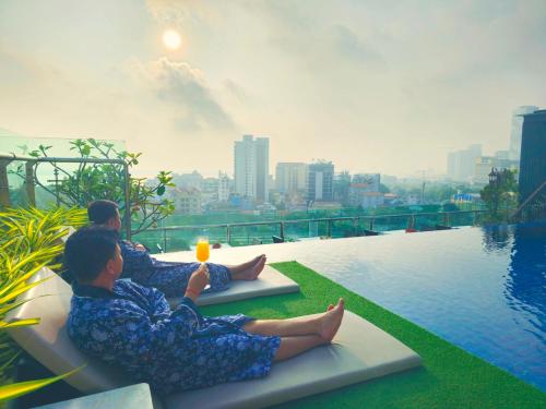 two people sitting on benches next to a swimming pool at Le Botum Hotel in Phnom Penh
