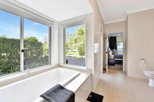 La salle de bains blanche est pourvue d'une baignoire et d'une fenêtre. dans l'établissement Lake Palm Resort Luxury Retreat absolute Waterfront on 3 acres at Lake Macquarie., à Dora Creek