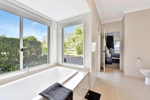 a white bathroom with a tub and a window at Lake Palm Resort Luxury Retreat absolute Waterfront on 3 acres at Lake Macquarie. in Dora Creek