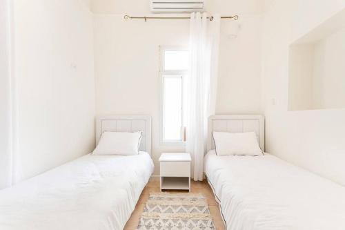 two beds in a room with white walls and a window at family home in acre in ‘Akko