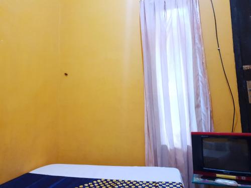 a bedroom with a bed and a tv and a curtain at SPOT ON 92857 Kos Haji Jakfar Syariah in Banyuwangi