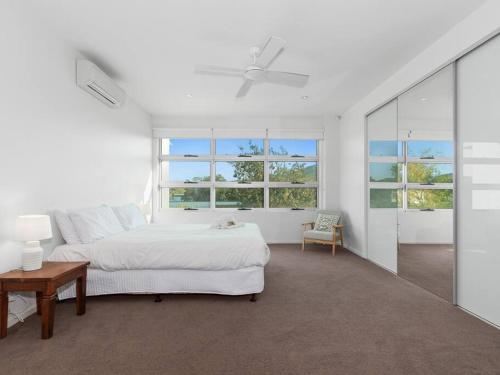 a white bedroom with a bed and a table and windows at Friday Island Cabarita in Cabarita Beach