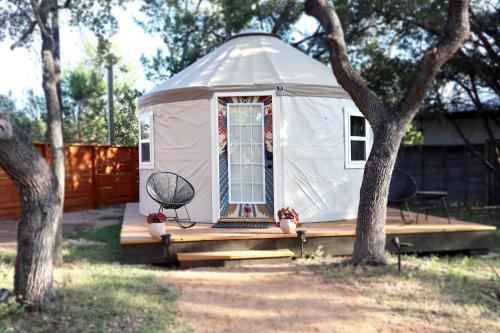 a yurt with a porch and a chair and two trees at Camposanto Glamping - The Macaw Yurt in Austin