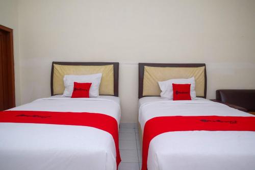 two beds with red pillows sitting next to each other at RedDoorz Syariah near Alun Alun Wonosari in Yogyakarta