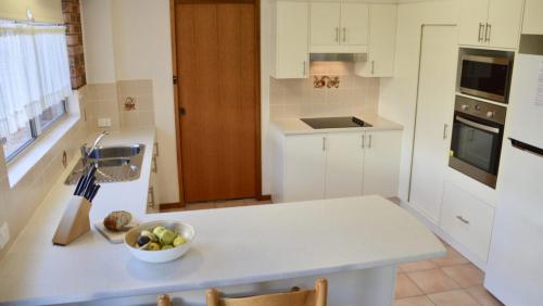 a white kitchen with a bowl of fruit on a counter at Lighthouse Palms in Ulladulla