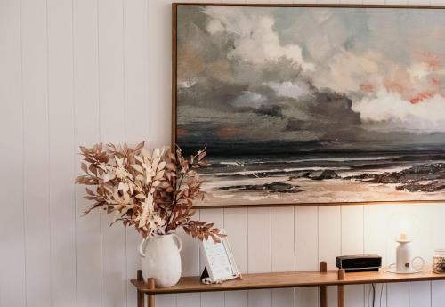 a vase of flowers on a shelf with a painting at Sweet Tide O Moyne in Port Fairy