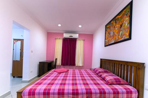 a pink bedroom with a bed with a plaid blanket at Vasudevam Premium Suites in Trivandrum