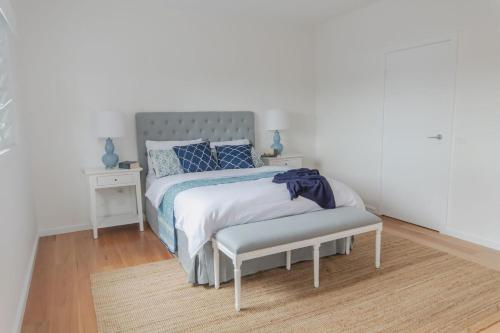 a white bedroom with a bed and a bench at Palm Tree Retreat in Mollymook
