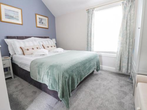 a bedroom with a bed with a green blanket and a window at Millgate Cottage in Conwy