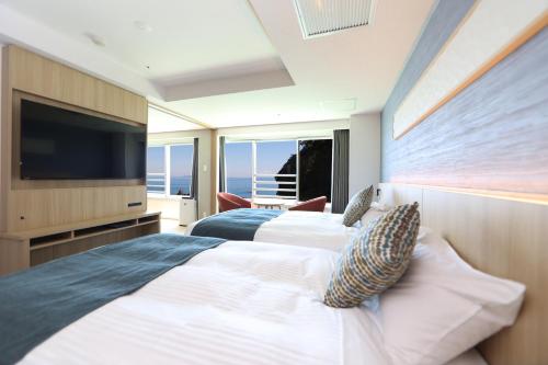 two beds in a room with a flat screen tv at Hotel New Akao in Atami