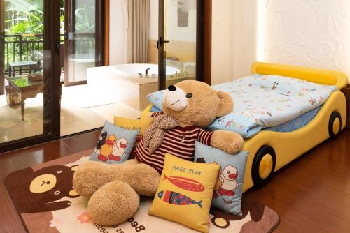a teddy bear sitting on the floor next to a bed at InterContinental Xishuangbanna Resort by IHG in Jinghong