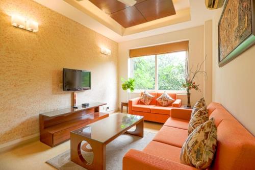 sala de estar con sofá naranja y TV en Ahuja Residency Noida, en Noida