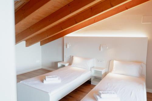 2 Betten in einem Zimmer mit weißen Wänden und Holzdecken in der Unterkunft LA CASA del TOMÀS in Pobla de Segur