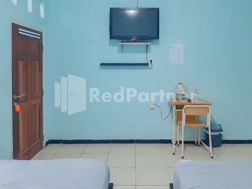 a blue room with a table and a tv on a wall at Syariah Safar Guest House Mitra RedDoorz in Cijoho