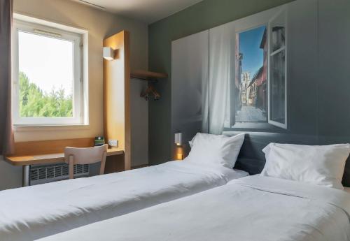 a bedroom with two beds and a desk and a window at B&B HOTEL Metz Jouy Aux Arches in Jouy-aux-Arches