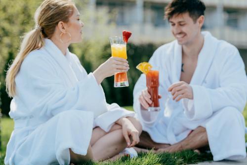 a man and woman sitting on the grass with drinks at Aqua Blu Hotel in Bad Füssing