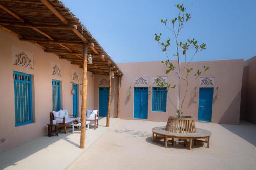 a patio with blue doors and a table with a tree at Nozol Al Rayaheen By Sharjah Collection in Khor Fakkan