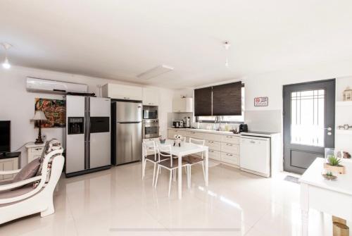 una cocina con electrodomésticos blancos, mesa y sillas en הבית בחורשה, en Zikhron Ya‘aqov