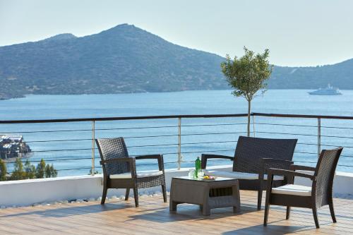 a deck with chairs and a table with a view of the water at Elounda Ilion Hotel Bungalows in Elounda