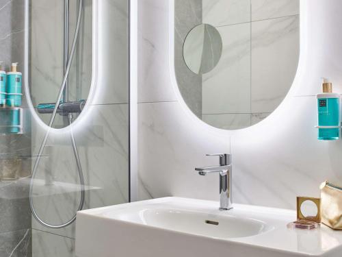 La salle de bains blanche est pourvue d'un lavabo et de deux miroirs. dans l'établissement Novotel Paris 13 Porte d'Italie, au Kremlin-Bicêtre