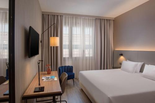 ein Hotelzimmer mit einem Bett, einem Schreibtisch, einem Bett und einem Fenster in der Unterkunft NH Trieste in Triest