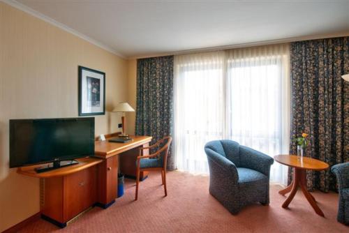 a hotel room with a desk and a television and a chair at Vital Hotel Westfalen Therme Wellness Resort & SPA in Bad Lippspringe