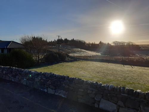 a stone wall and a field with the sun in the background at Kelly's Pod in Garynahine