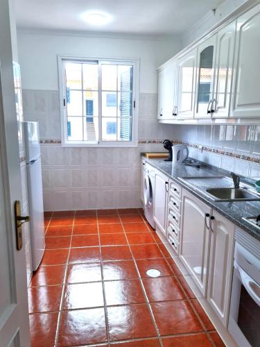 a kitchen with white cabinets and a red tile floor at Abrigo das Matas in Porto Santo