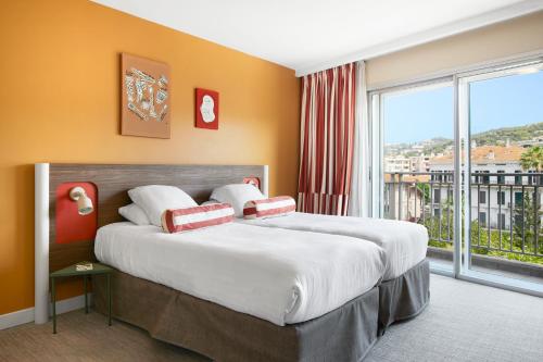 a bedroom with a large bed and a large window at Hotel Abrial in Cannes