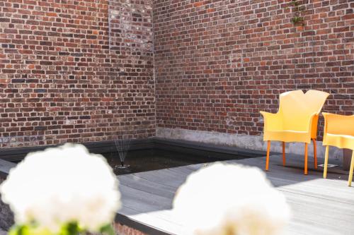 a patio with yellow chairs and a brick wall at Vakantiewoning & Fietslogies V E L O, Tussen Hasselt en Maastricht in Bilzen