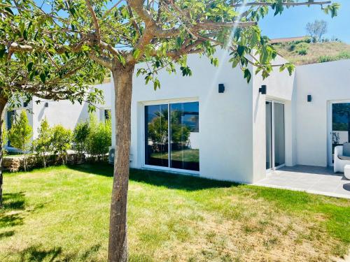 a white house with a tree in the yard at Bella Vista Hôtel, Suites & Maisons in Porticcio