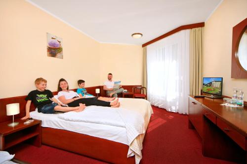 tres personas sentadas en una cama en una habitación de hotel en Wellness Hotel Svornost en Harrachov